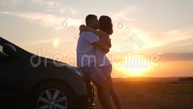 幸福夫妇的剪影停留在新车的天空下。 日落时分，美丽的年轻夫妇站在汽车附近。